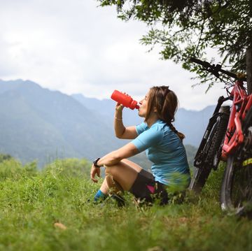 young woman with mountain bike on italian mountains drinking water