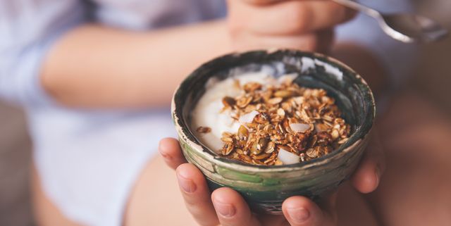 Young woman with muesli bowl. Girl eating breakfast cereals with nuts, pumpkin seeds, oats and yogurt in bowl. Girl holding homemade granola. Healthy snack or breakfst in the morning.