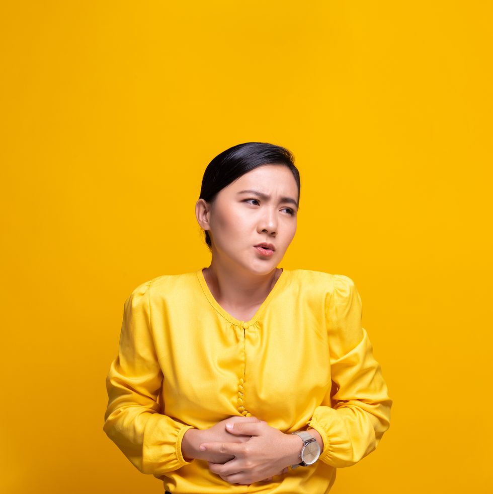 young woman with stomachache against yellow background