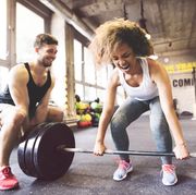 young woman with training partner preparing to lift barbell in gym