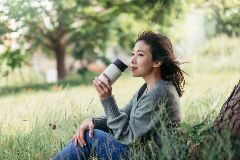young woman with travel mug sitting in meadow