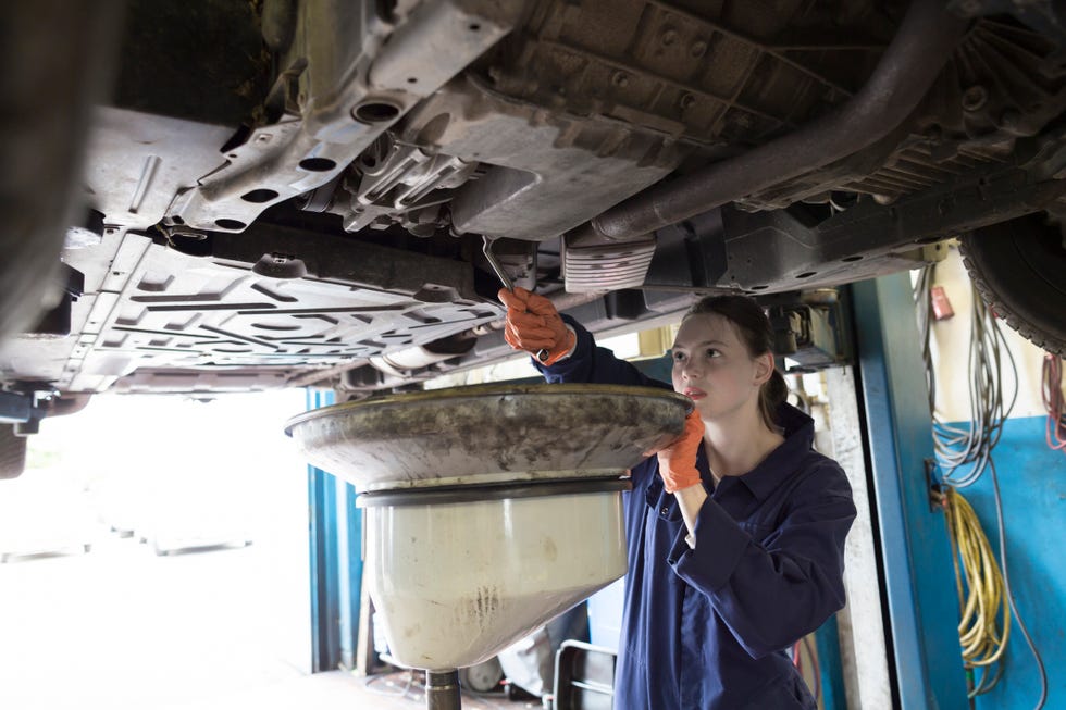 Молодая женщина, работающая в ремонтном гараже, меняет масло