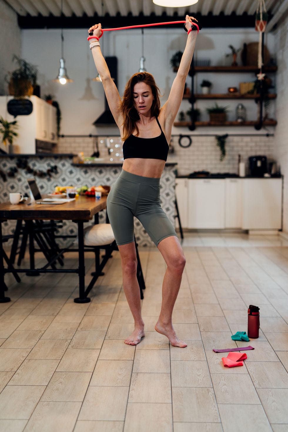 young woman working out at home doing overhead resistance band stretch