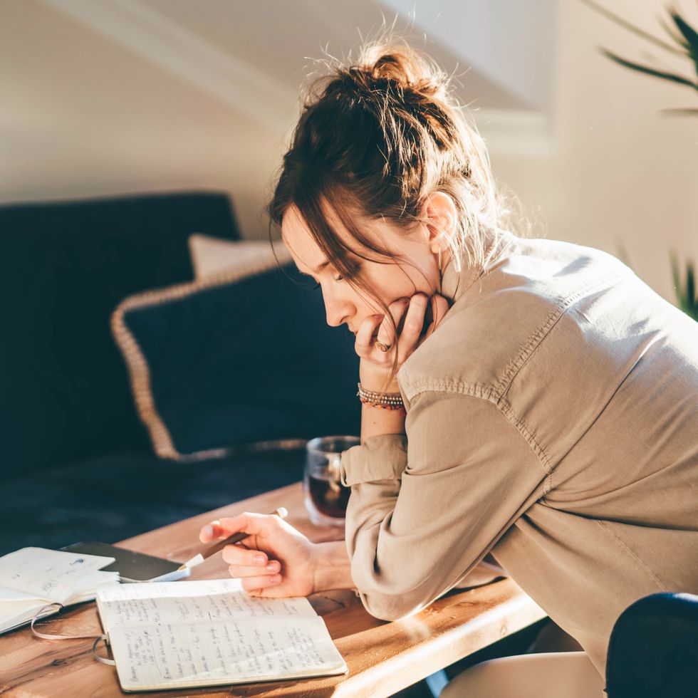 young woman writes in notebook at apartment.