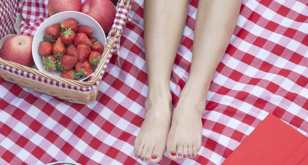 young woman's feet on a checkered blanket with a picnic basket, shoes, and a book
