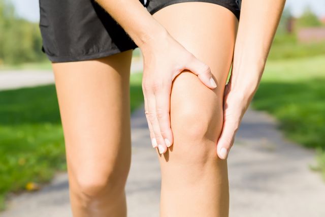 young woman's hand touching her knee during running time on footpath joint pain sporty problem and solution close up front view