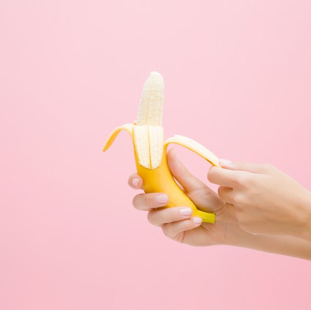 young woman's hands peeling a beautiful, fresh, yellow banana on pastel pink background healthy sweet summer food side view