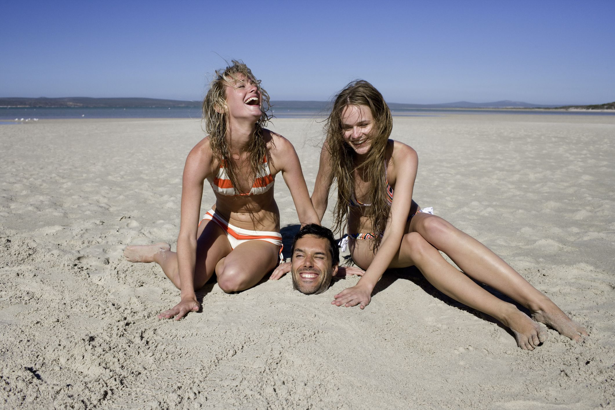 young women burying man in sand laughing royalty free image 1677187269