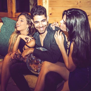 young women flirting with man while sitting with him on sofa in party