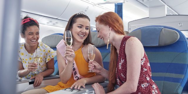 Young women friends laughing, drinking champagne in first class on airplane