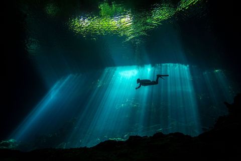 Een zuil van licht valt op een duiker in een cenote Wanneer je in een cenote duikt schrijft Guerin word je een avonturier en archeoloog omdat je achter elke rots iets nieuws ontdekt