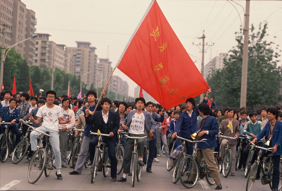Een groep Chinese studenten rijdt op de fiets door Beijing zwaaiend met banieren en burgers oproepend om hun beweging voor meer democratie te steunen