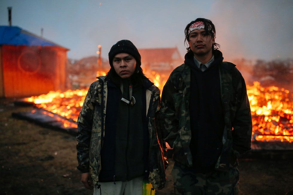 Twee jonge activisten voor de waterrechten van indianen staan voor de verkoolde resten van een hogan een traditionele Navajohut in Cannon Ball North Dakota Maandenlang bezetten de demonstranten het reservaat van Standing Rock uit protest tegen de aanleg van de Dakota Access Pipeline Toen ze in februari 2017 moesten vertrekken staken sommige activisten delen van het protestkamp in brand