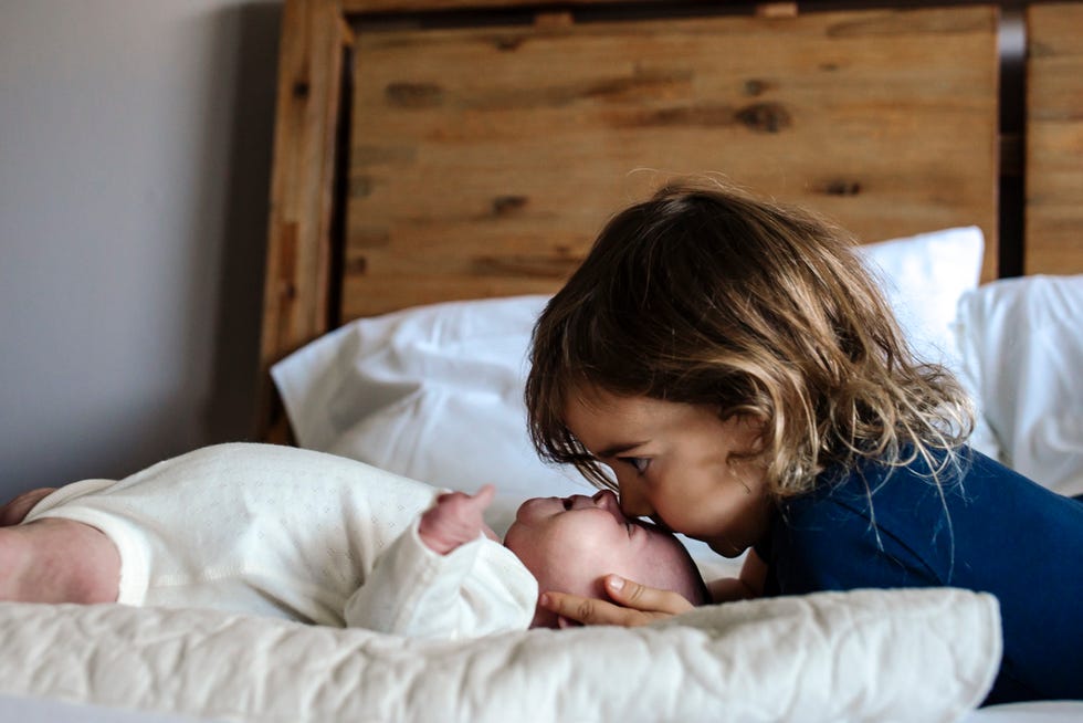 4 yr old kissing head of newborn sister on bed with pillows