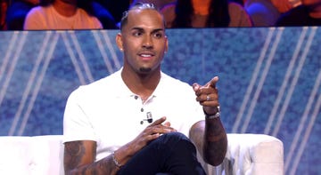 a person gesturing while seated on a couch during a discussion or talk show