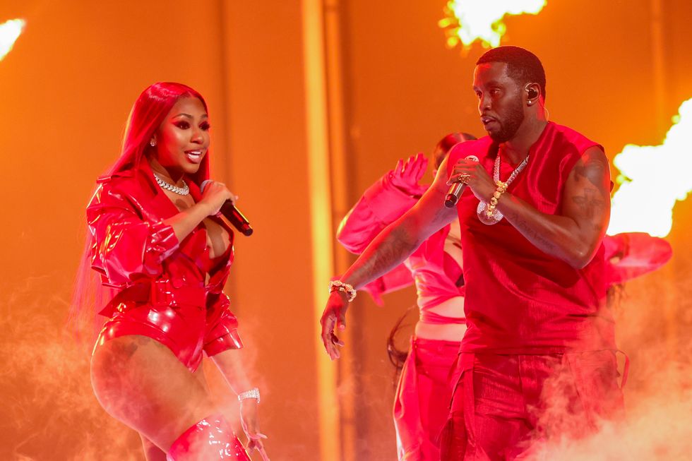 yung miami and sean diddy combs sing into microphones they hold while moving around on a stage, both wear red outfits