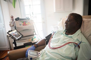 a man sitting in a chair with several tubes attached carrying blood to a large machine