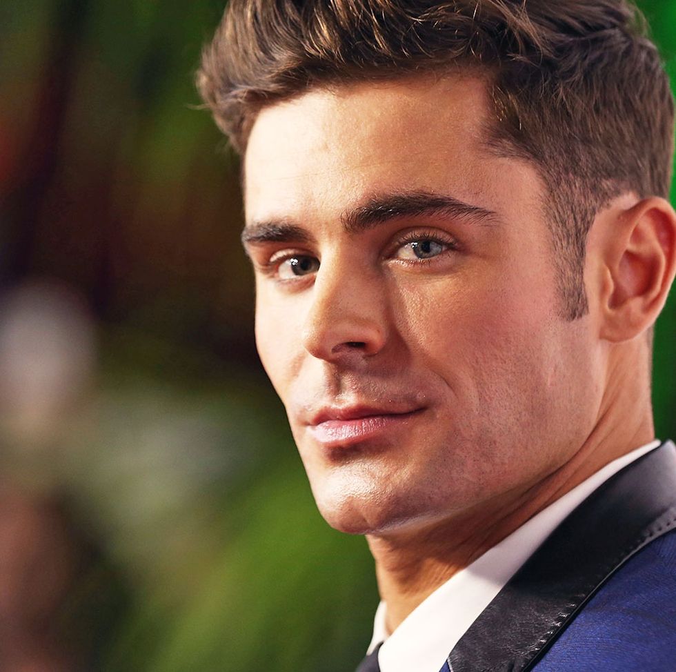 zac efron wears a suit and looks over his shoulder at the camera