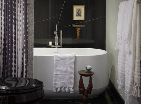 kohler white bathtub with white bath mat, black floor to ceiling marble wall tiles