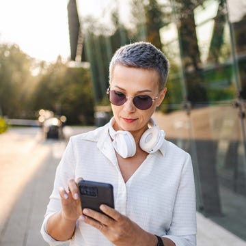 zapatillas barefoot una mujer usa su teléfono móvil mientras camina y lleva colgados al cuello unos auriculares inalámbricos