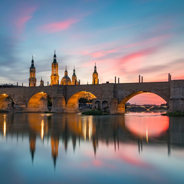 view of the medieval puente de piedra bridge leading up to the basilica of our lady of the pilla, the iconic basilica in zarogoza, spain