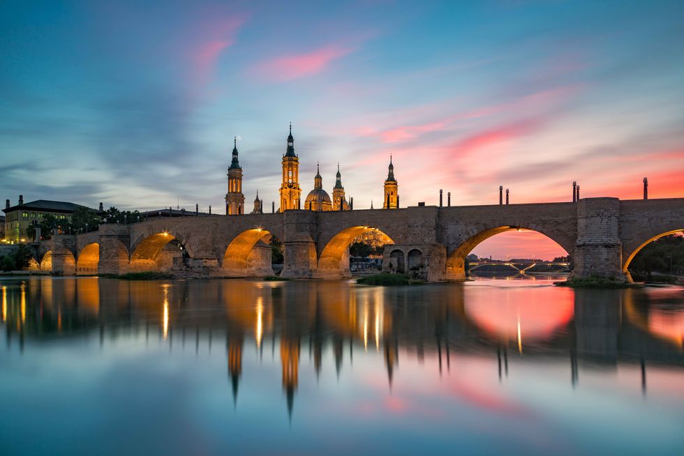 view of the medieval puente de piedra bridge leading up to the basilica of our lady of the pilla, the iconic basilica in zarogoza, spain