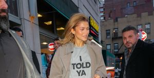 zendaya wearing loewes i told ya t shirt in the colour grey and black lettering with a beige trench coat on top and black trousers and cream shoes