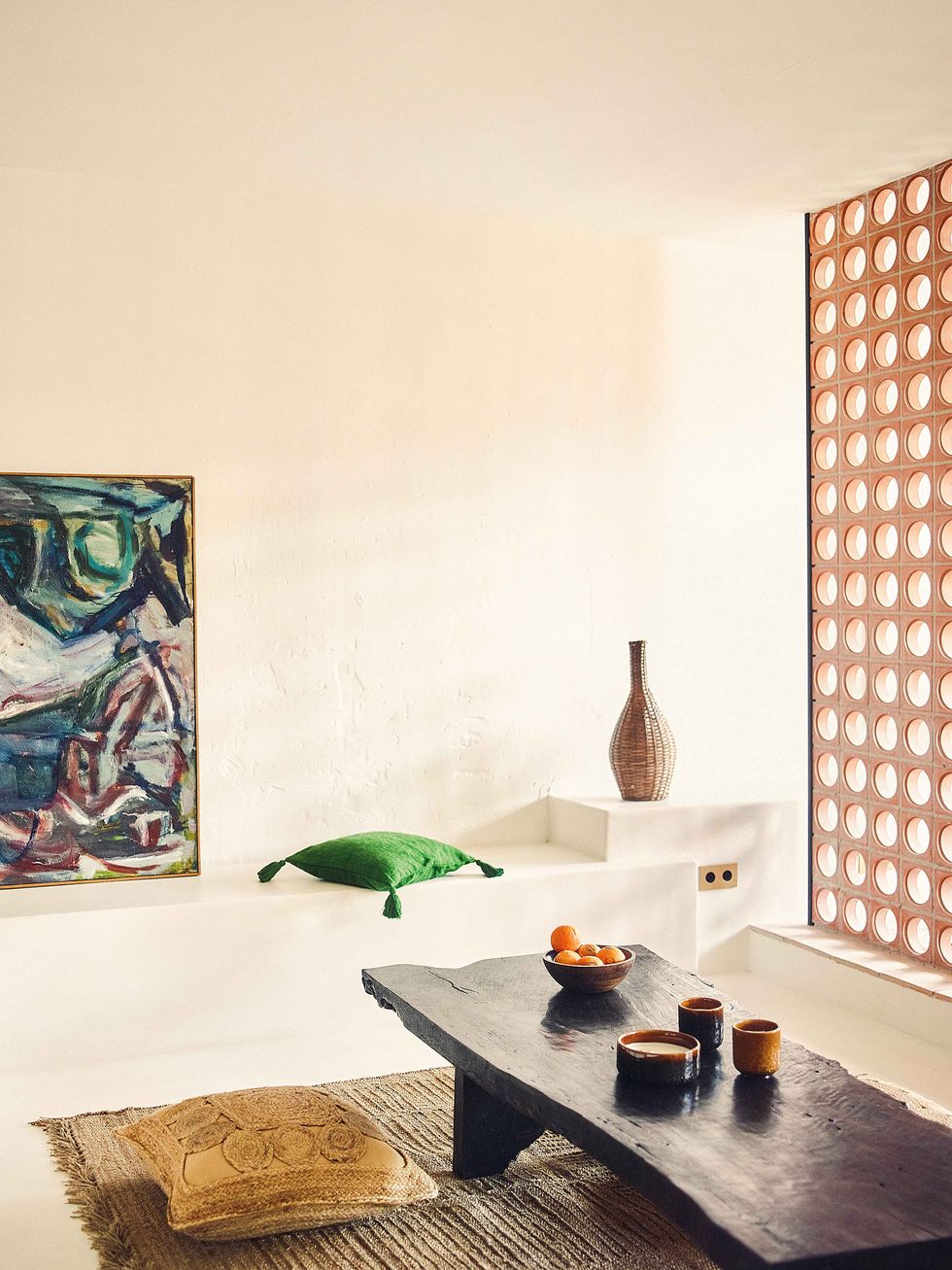 salón de estilo artesanal y mediterráneo con mesa baja de madera oscura y alfombra de fibras naturales, con un fondo y pared blancos