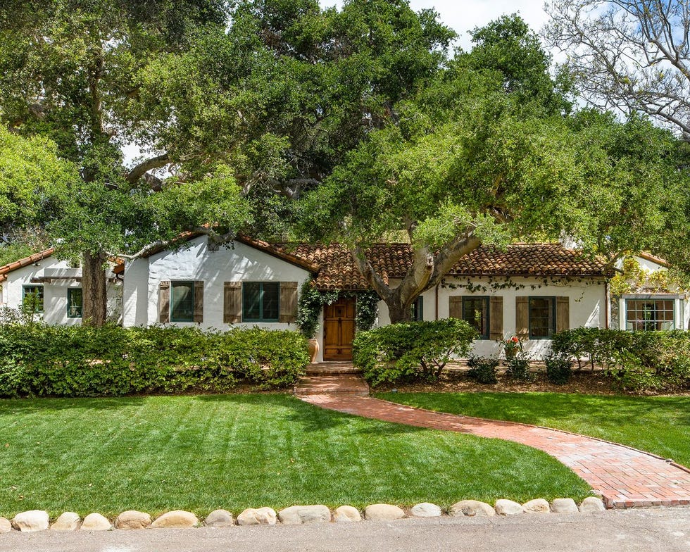 singlestory house surrounded by greenery with a brick pathway