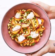 zipper peas with peaches and burrata in a pink bowl held by two hands