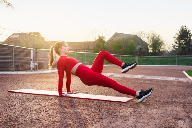 vrouw doet omgekeerde plank op atletiekbaan bij ondergaande zon