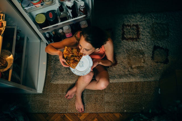 vrouw eet 's nachts een pizza voor de koelkast