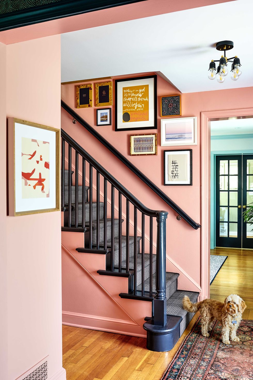 pink painted entryway with black staircase banister and dark gray checkered stair runner, gallery wall