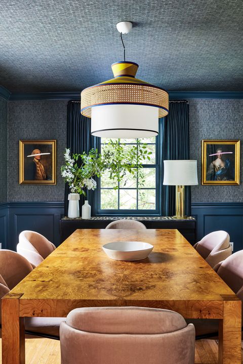 brown dining table, pink velvet cushioned dining chairs, blue painted walls with dark blue wall covering, wall art in gold frames