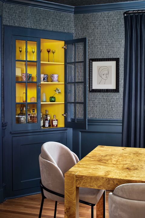 dining room with blue painted walls and dark blue wall covering, bar cabinet with alcohol,  wooden dining chair with pink velvet dining chairs