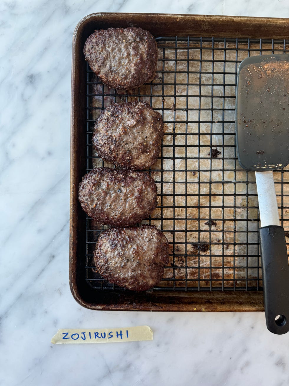 four cooked hamburger patties arranged on a wire cooling rack set inside a baking tray