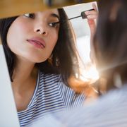 hispanic woman applying mascara in mirror