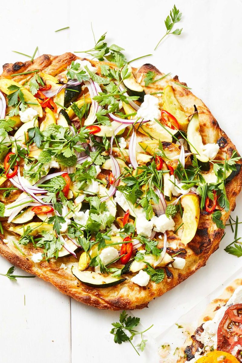 zucchini squash pizza with slices of red onion and herbs on top