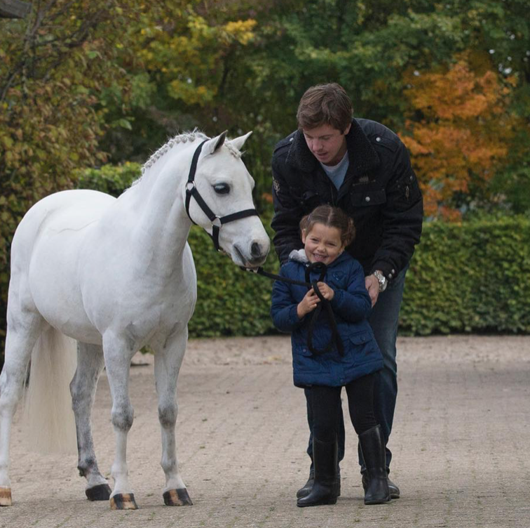 a person and a child petting a white horse