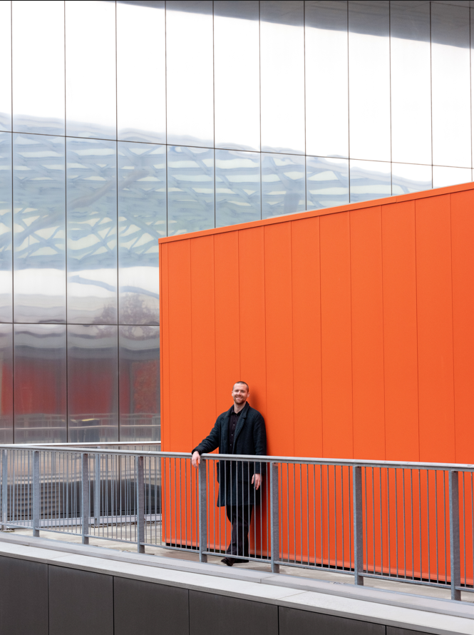 a man standing in front of a large orange wall