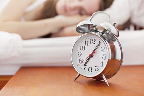 Woman sleeping with alarm clock on bedside table
