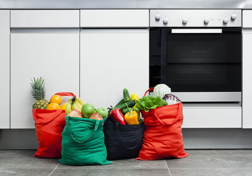 Reusable shopping bags filled with fruit and vegetables in a kitchen.