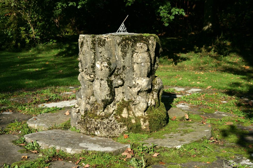 Stone sundial with Winnie the Pooh engravings in sunlight in green garden