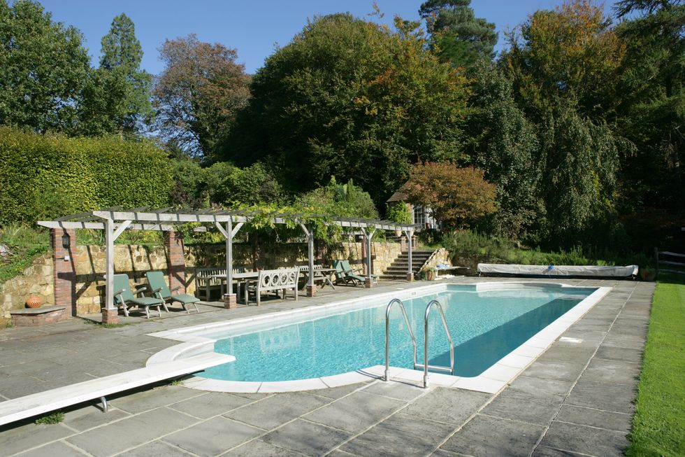 Shaped outside swimming pool in large garden with outside furniture