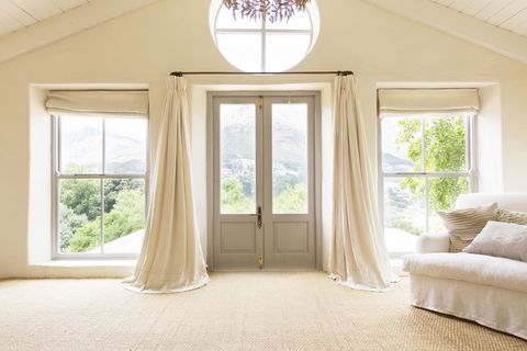 Light room with set of doors, white curtains and furniture looking out into the countryside