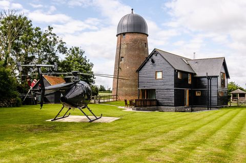 Brick tower mill attached to black house with green gardens and helicopter