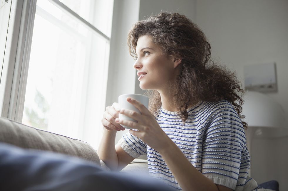 Smiling young woman with cup of coffee looking out of window