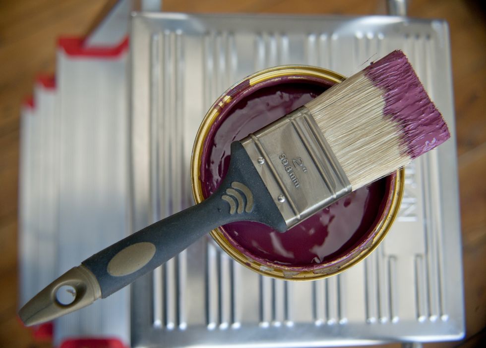 Paint brush dipped in paint balanced on pot of paint and stepladder