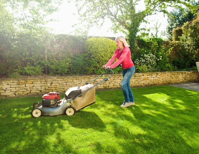 Woman mowing sunlit garden lawn with lawn mower