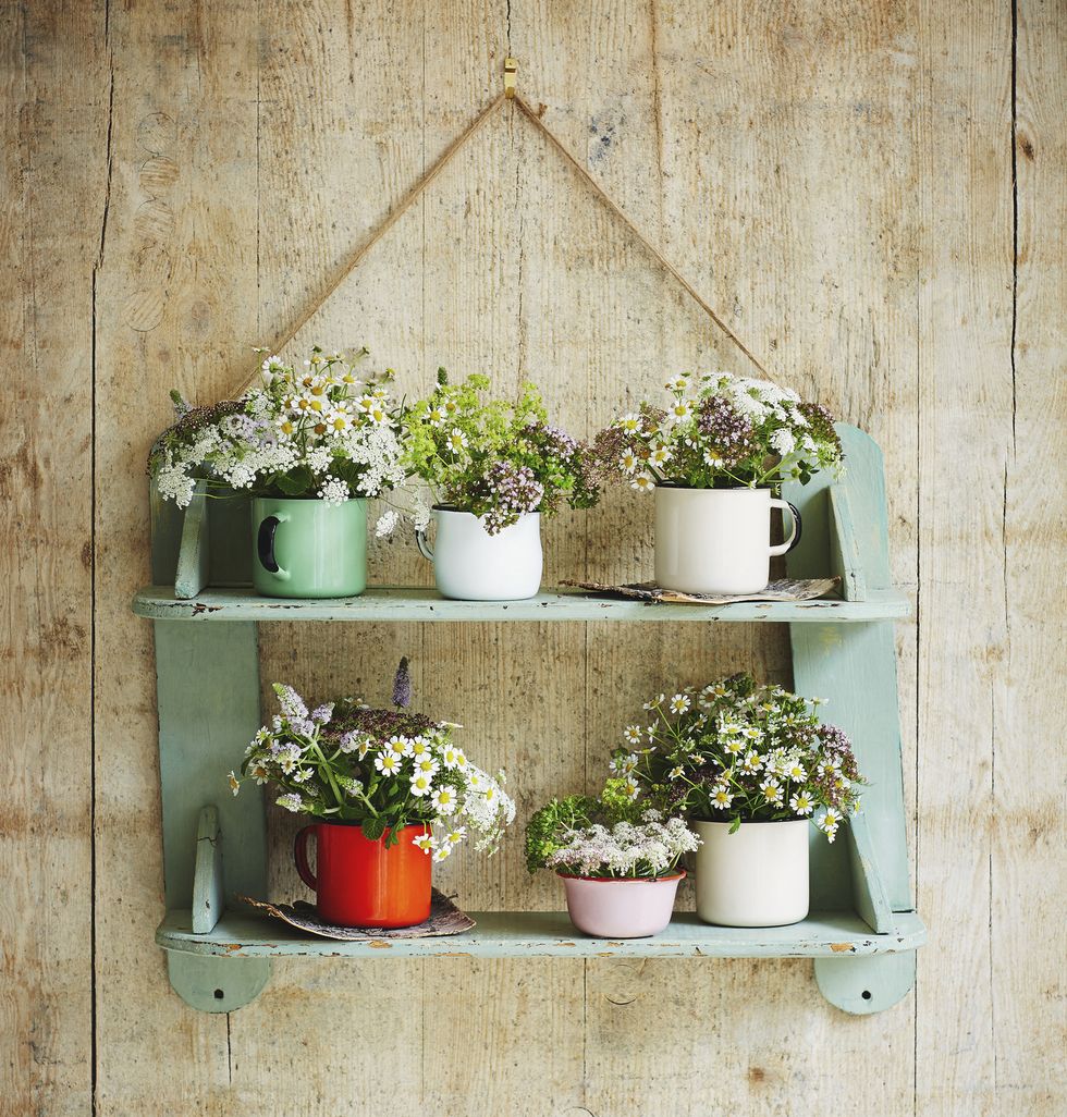 Hanging shelf with enamel mugs containing flowers